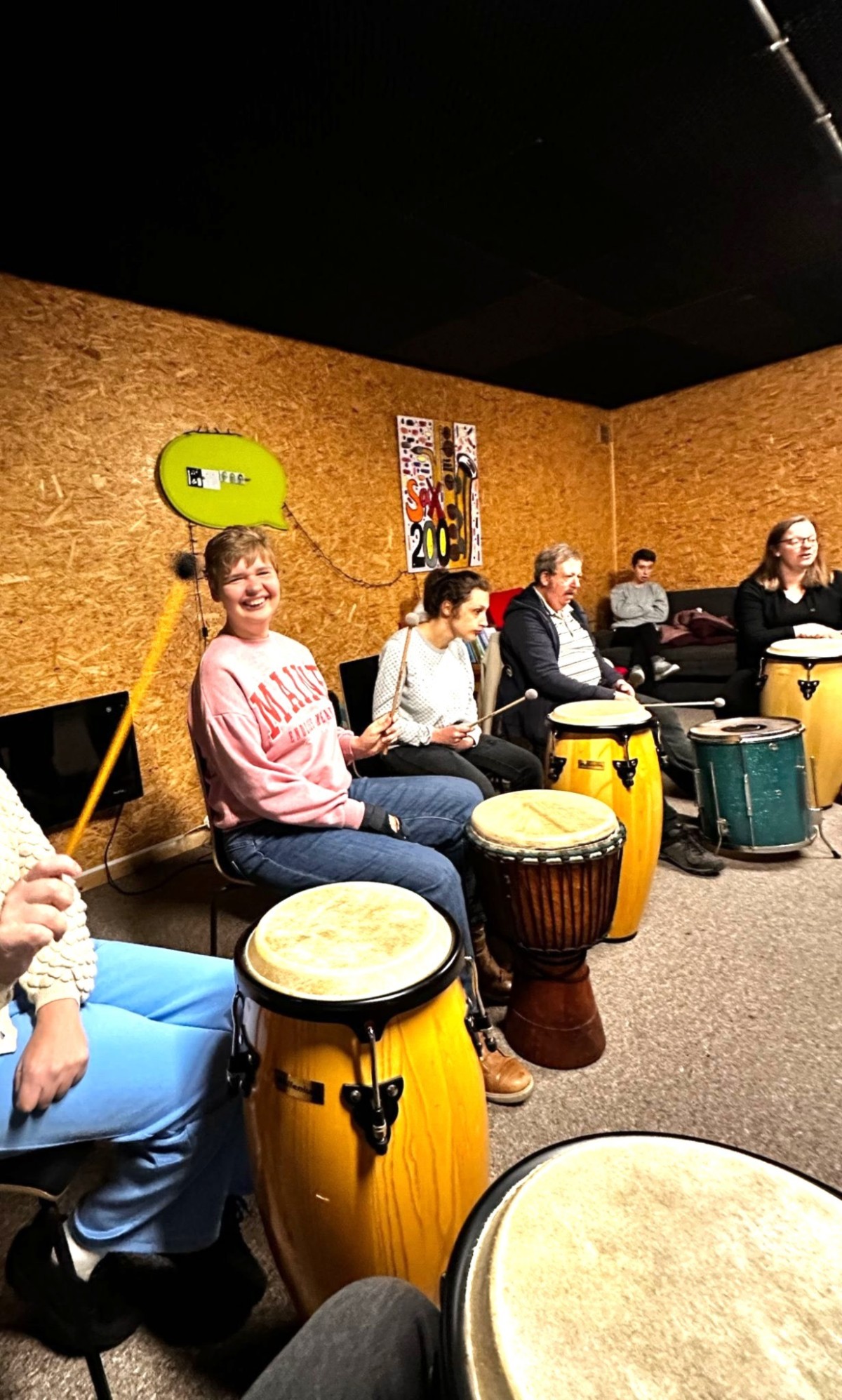Een groep mensen zit in een muzikale ruimte en speelt op verschillende percussie-instrumenten, zoals conga's en djembe's.