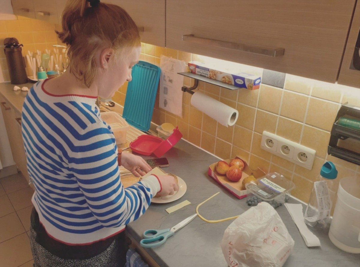 Een persoon met een standaard gestreepte trui staat in een keuken en bereidt voedsel op een aanrecht, omringd door verschillende keukenspullen en ingrediënten.