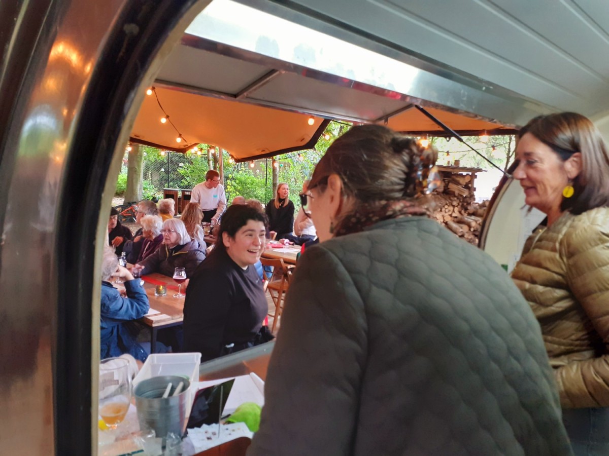 Groep mensen in een bistro-achtige setting met vrolijke gesprekken, een achtergrond met houten meubels en sfeervolle verlichting.